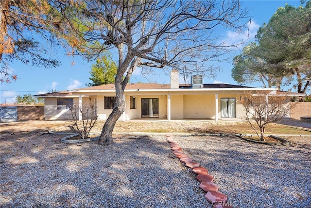 view of front facade featuring stucco siding, a patio, a chimney, and fence