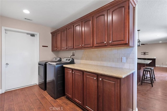 clothes washing area featuring dark wood-type flooring, washing machine and dryer, cabinet space, and visible vents