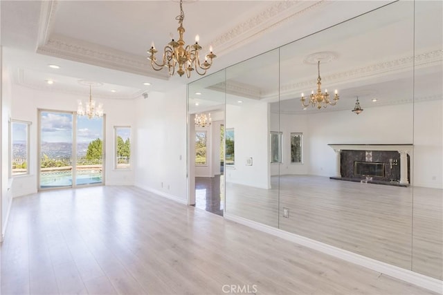 unfurnished living room featuring a high end fireplace, crown molding, wood finished floors, a notable chandelier, and a raised ceiling