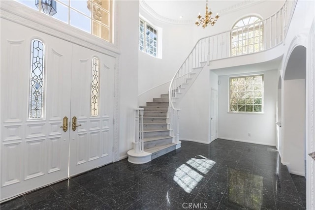 foyer entrance featuring stairway, baseboards, granite finish floor, a towering ceiling, and a notable chandelier