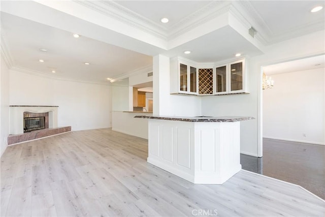 kitchen featuring a high end fireplace, light wood-style floors, white cabinets, crown molding, and glass insert cabinets