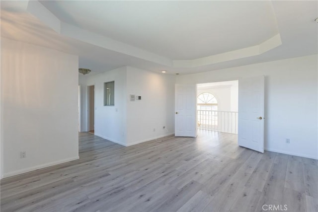 spare room featuring a raised ceiling, baseboards, and light wood-type flooring