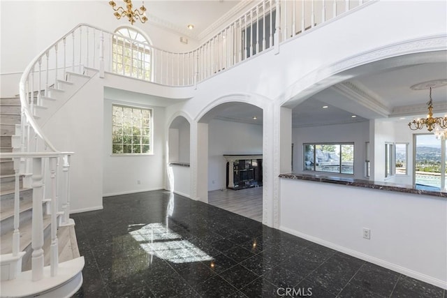 unfurnished living room with baseboards, a high ceiling, granite finish floor, crown molding, and a chandelier