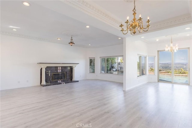 unfurnished living room featuring a high end fireplace, crown molding, baseboards, light wood-style floors, and a notable chandelier