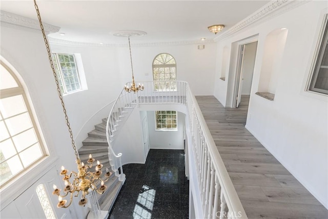 foyer entrance with a high ceiling, a notable chandelier, a healthy amount of sunlight, and crown molding