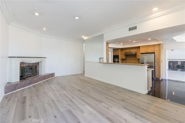 unfurnished living room featuring visible vents, wood finished floors, a high end fireplace, and crown molding