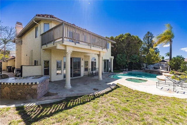 rear view of property featuring a balcony, an in ground hot tub, a chimney, stucco siding, and a patio area