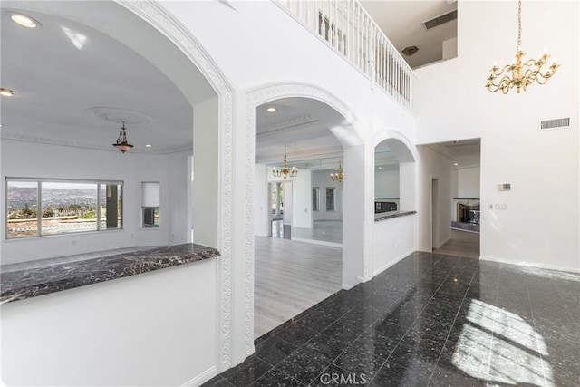 hallway with visible vents, baseboards, a chandelier, a high ceiling, and granite finish floor