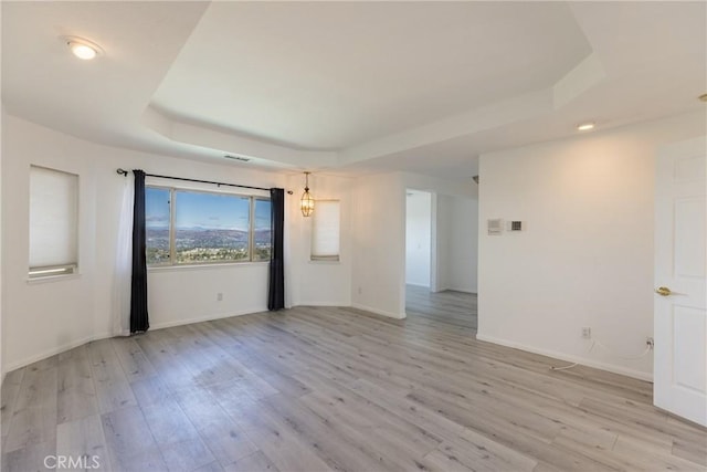 unfurnished room with light wood-type flooring, a raised ceiling, baseboards, and visible vents