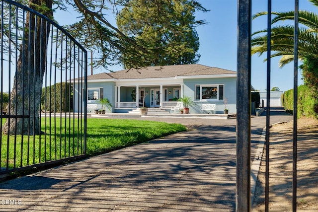 view of front of house with stucco siding, a porch, a front lawn, and fence