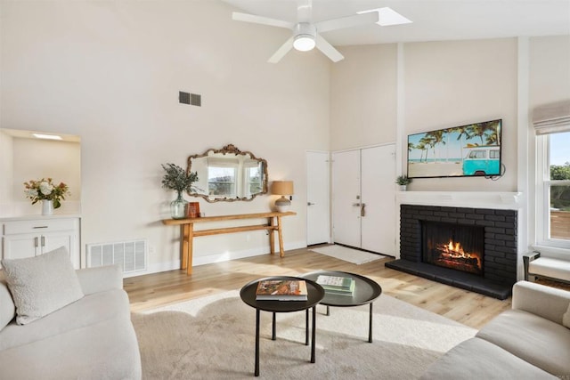 living area featuring a brick fireplace, visible vents, light wood finished floors, and high vaulted ceiling