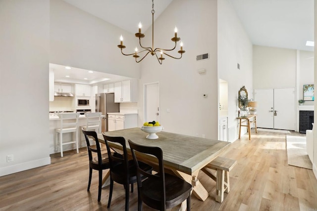 dining space with light wood finished floors, visible vents, baseboards, an inviting chandelier, and high vaulted ceiling