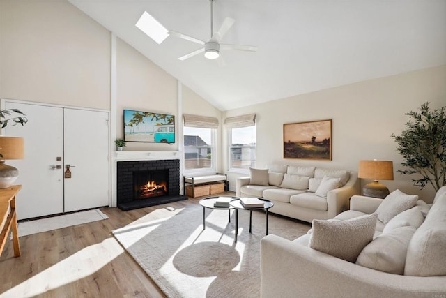 living area featuring a fireplace, a skylight, wood finished floors, high vaulted ceiling, and a ceiling fan