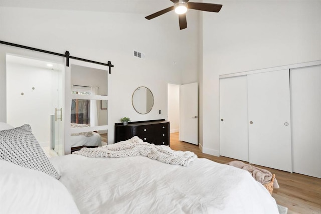 bedroom featuring visible vents, high vaulted ceiling, wood finished floors, a barn door, and a closet