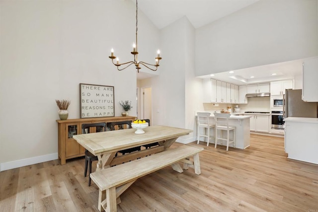 dining space with baseboards, light wood finished floors, a high ceiling, recessed lighting, and a chandelier