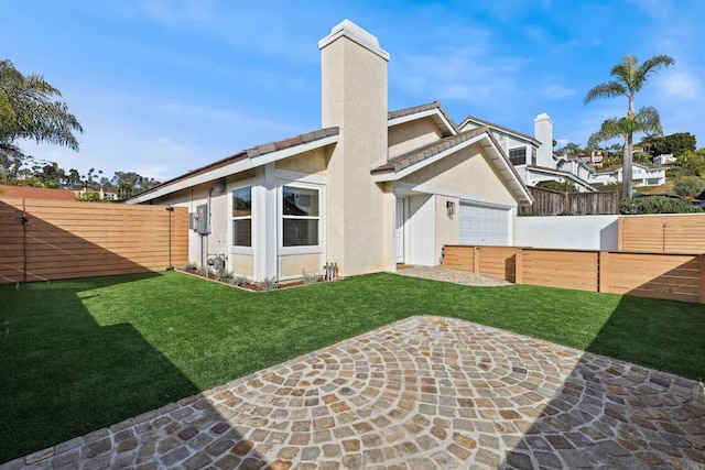 back of house with a chimney, stucco siding, a lawn, and a fenced backyard