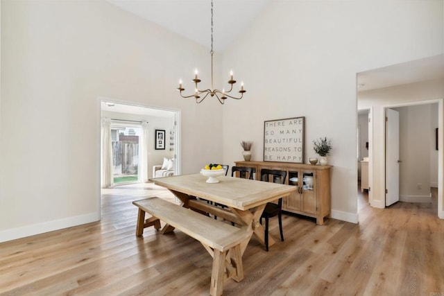 dining space featuring a notable chandelier, baseboards, high vaulted ceiling, and light wood finished floors