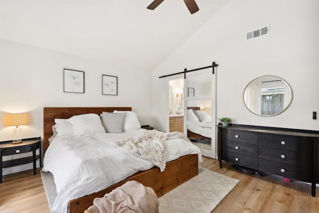 bedroom featuring visible vents, ceiling fan, light wood-style floors, a barn door, and connected bathroom