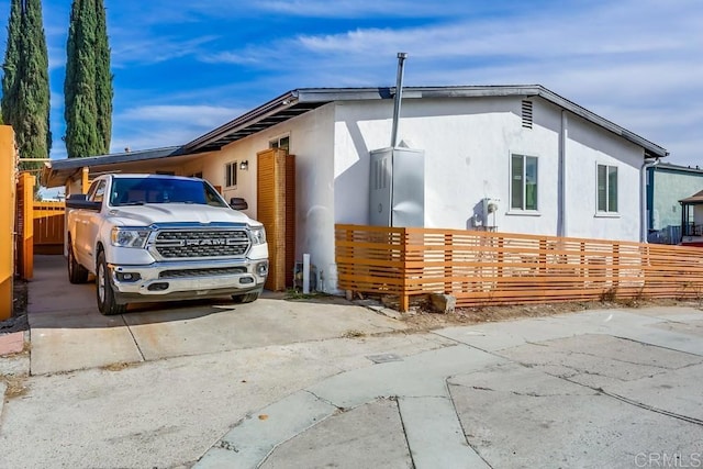 view of side of property with fence, driveway, and stucco siding