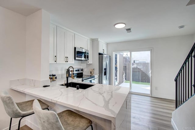 kitchen featuring light stone countertops, a peninsula, light wood-style flooring, a sink, and appliances with stainless steel finishes