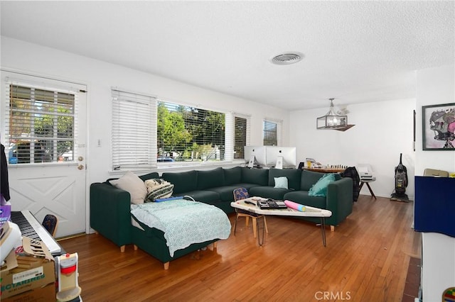 living room with an inviting chandelier, wood finished floors, visible vents, and a textured ceiling