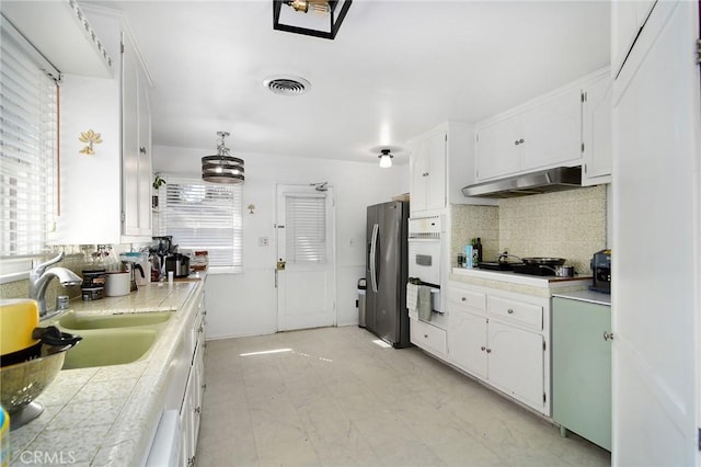 kitchen with visible vents, oven, a sink, under cabinet range hood, and stainless steel fridge