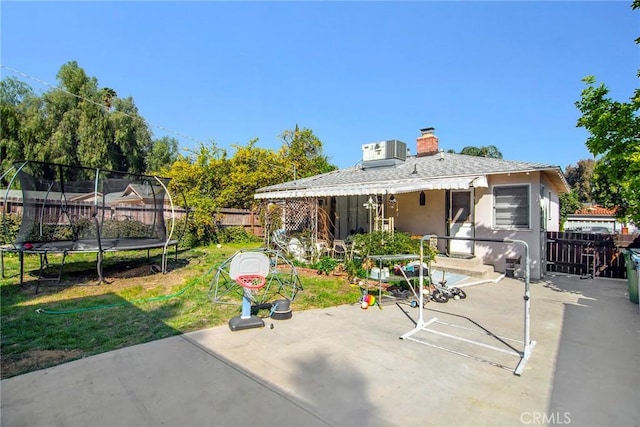 back of house featuring a trampoline, stucco siding, a fenced backyard, a yard, and a patio area