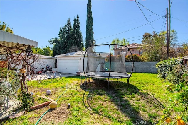 view of yard featuring an outbuilding, a detached garage, a trampoline, and fence