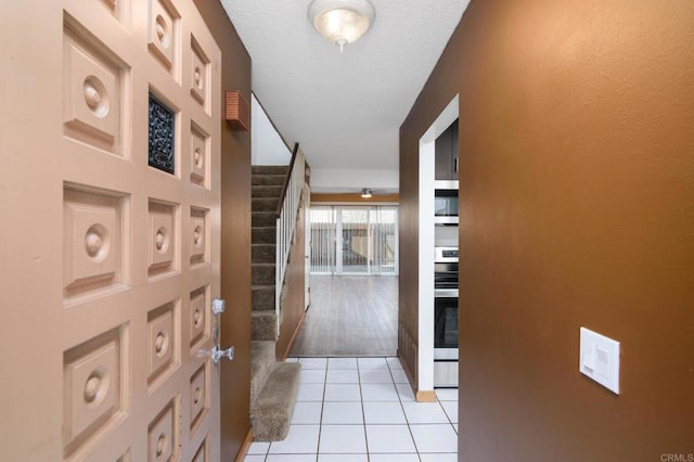 corridor with stairway, light tile patterned flooring, and a textured ceiling