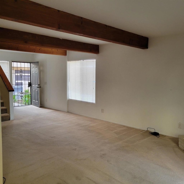 carpeted empty room with stairs and beam ceiling