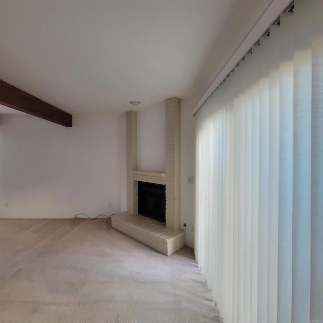 unfurnished living room with a brick fireplace, beamed ceiling, and light carpet