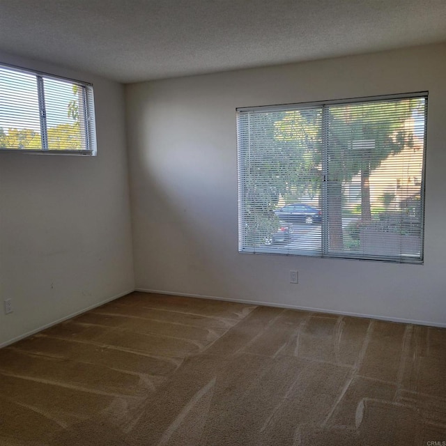 carpeted spare room featuring a textured ceiling and baseboards