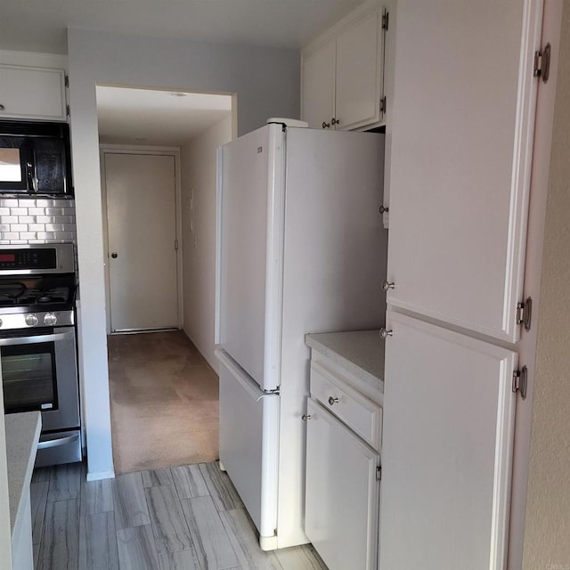 kitchen featuring black microwave, light countertops, stainless steel gas range, freestanding refrigerator, and white cabinetry