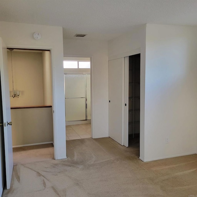 unfurnished bedroom featuring carpet flooring, a textured ceiling, ensuite bathroom, and visible vents