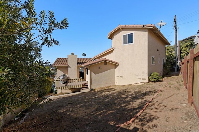 back of property featuring fence, a chimney, stucco siding, a deck, and a tiled roof