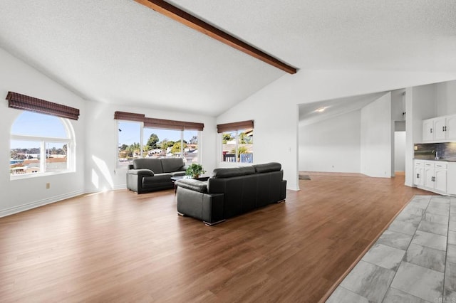 living area with light wood-style flooring, vaulted ceiling with beams, a healthy amount of sunlight, and a textured ceiling