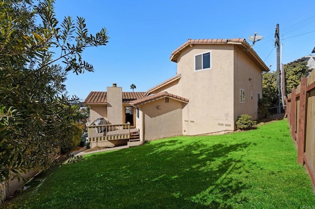 back of house featuring stucco siding, a lawn, a tile roof, fence, and a chimney