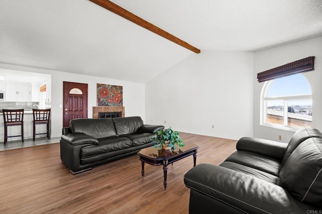 living area with a tiled fireplace, vaulted ceiling with beams, baseboards, and wood finished floors