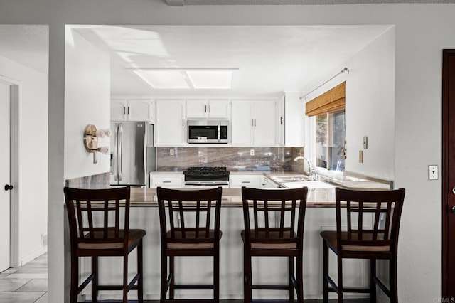 kitchen with a sink, white cabinetry, stainless steel appliances, a peninsula, and decorative backsplash