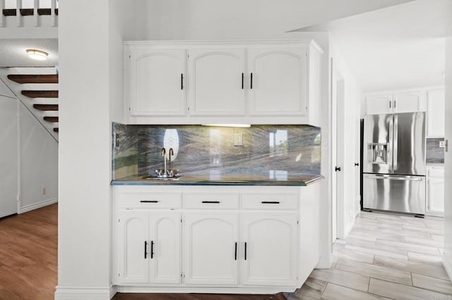 kitchen with a sink, stainless steel fridge, white cabinets, light wood-style floors, and tasteful backsplash