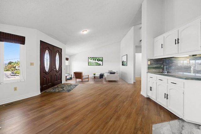 foyer featuring vaulted ceiling, wood finished floors, visible vents, and baseboards