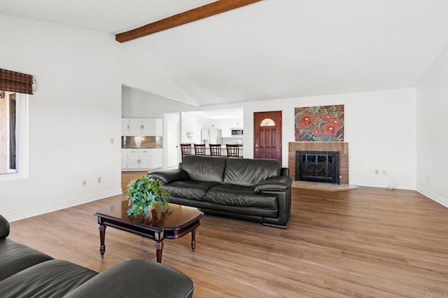 living area featuring light wood-type flooring, beamed ceiling, high vaulted ceiling, baseboards, and a brick fireplace