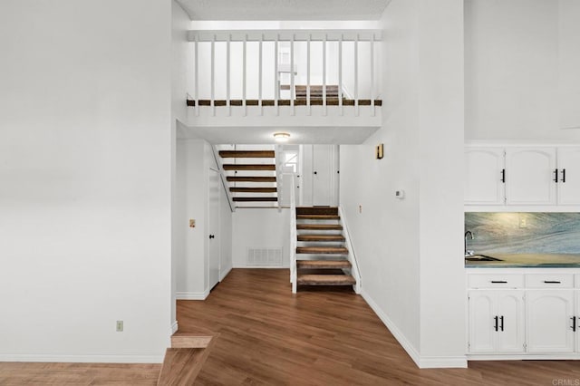 staircase with visible vents, baseboards, a towering ceiling, and wood finished floors