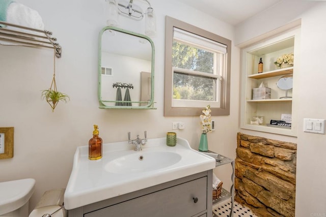 half bathroom featuring visible vents, toilet, built in shelves, and vanity