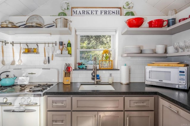 kitchen with dark countertops, backsplash, open shelves, white appliances, and a sink