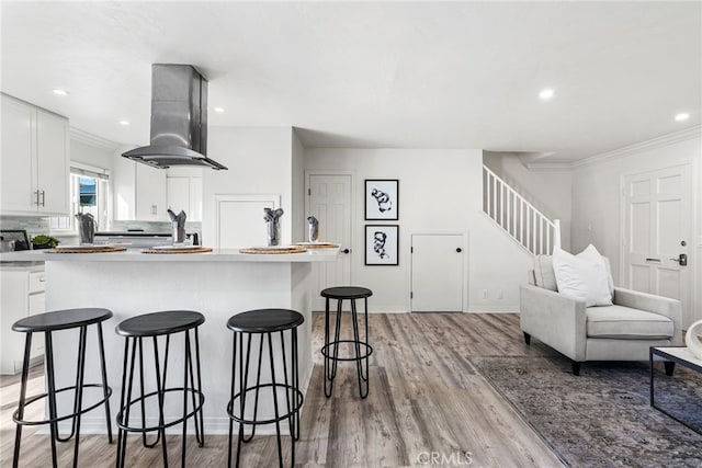 kitchen featuring light wood-type flooring, a kitchen bar, island exhaust hood, a kitchen island, and white cabinetry