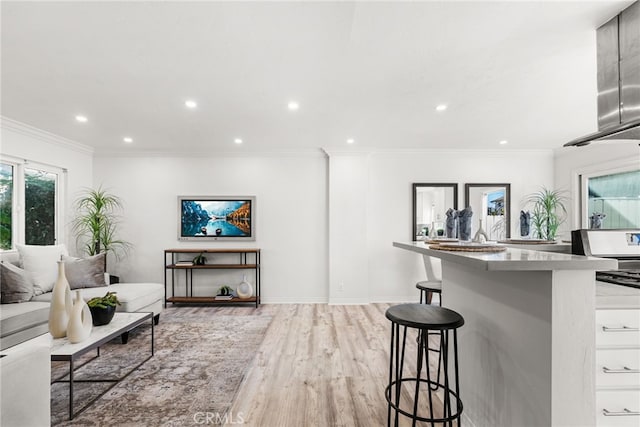 interior space with a breakfast bar, recessed lighting, ornamental molding, light countertops, and light wood-style floors