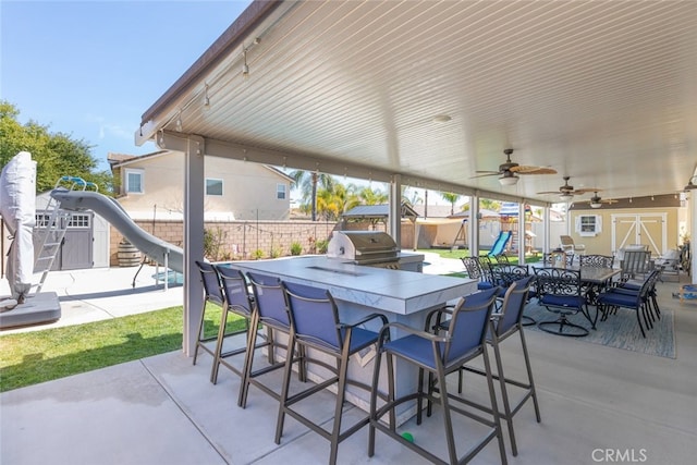 view of patio / terrace with outdoor dry bar, a playground, fence, an outbuilding, and area for grilling