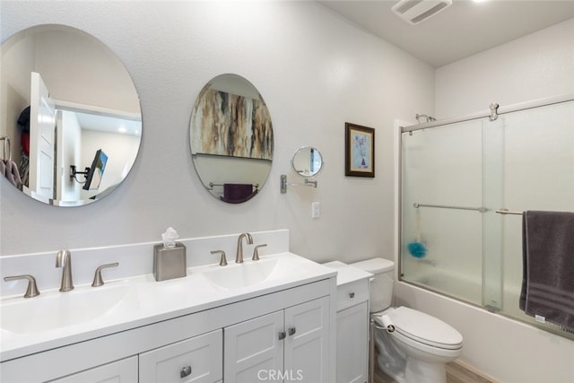 full bathroom with visible vents, toilet, double vanity, enclosed tub / shower combo, and a sink