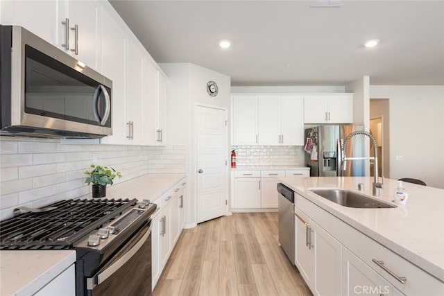 kitchen with a sink, tasteful backsplash, light wood-style floors, appliances with stainless steel finishes, and white cabinets